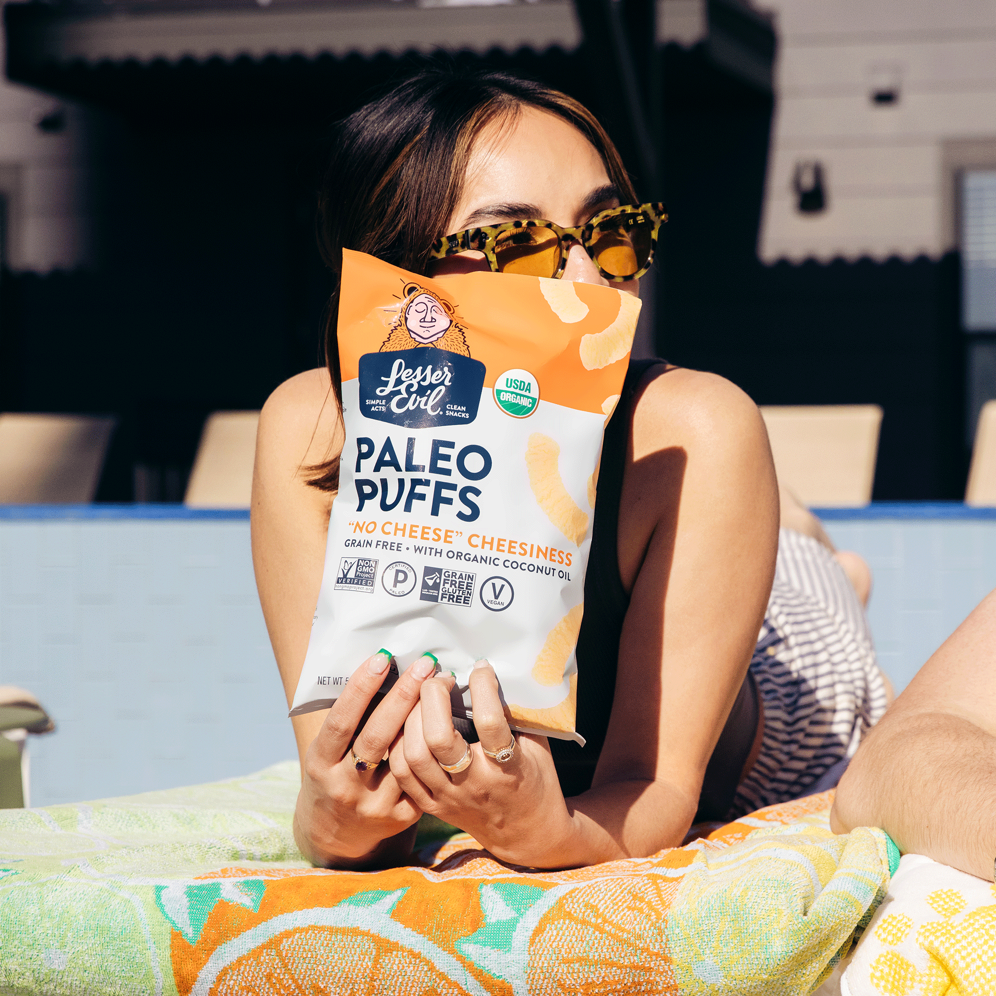 woman on beach towel holding bag of cheese paleo puffs